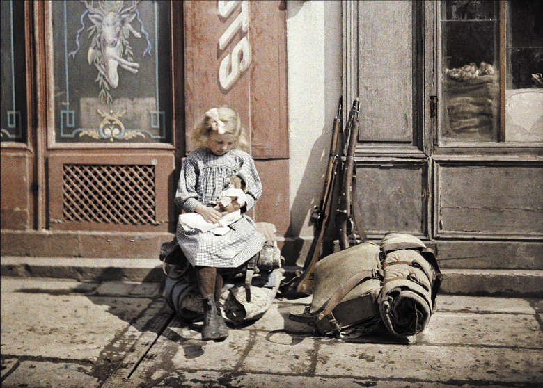 A little girl playing with her doll; two guns and a knapsack are next to her on the ground, Reims, Marne, France, 1917 (autochrome) Fernand Cuville (1887-1927) 